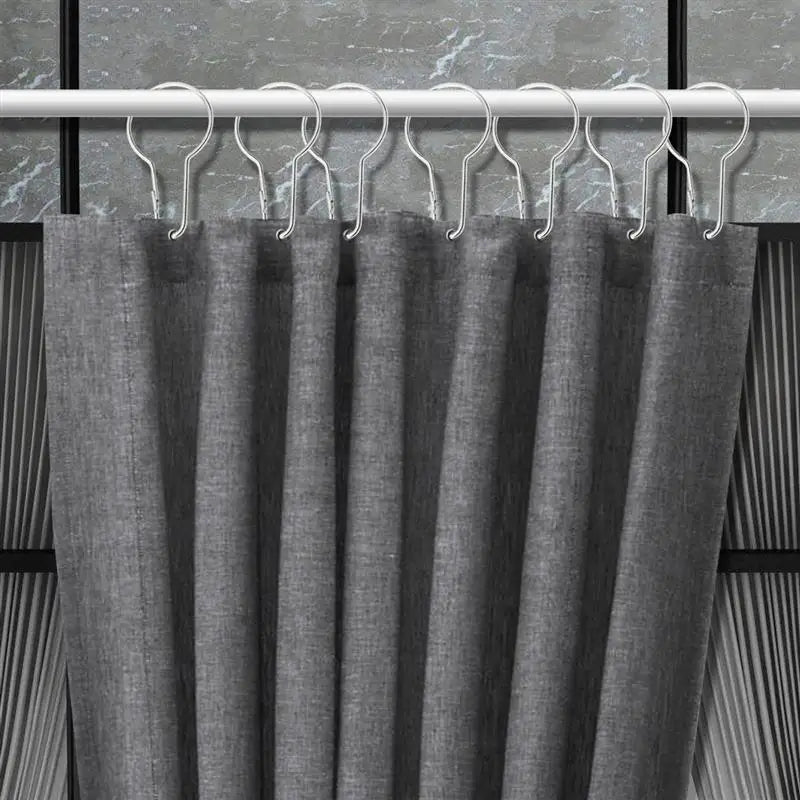 Crochets métalliques fixés à un rideau gris foncé sur une tringle, montrant leur compatibilité avec les rideaux épais.