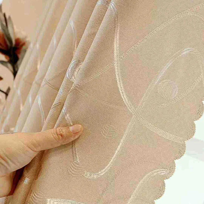 Main tenant un rideau beige jacquard au motif courbé et lumineux, avec finition festonnée sur le bord.