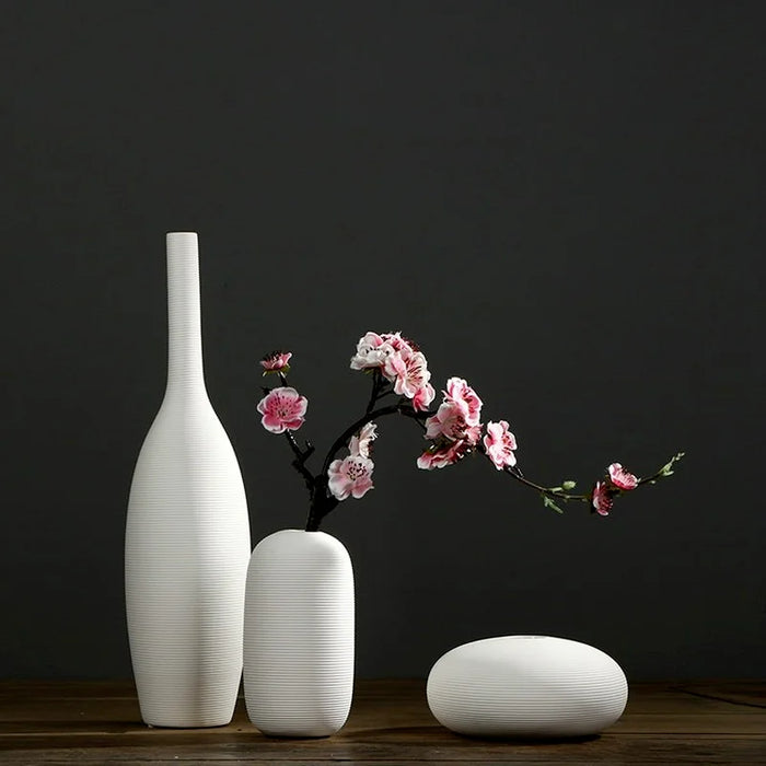 Des vases blancs élégants et épurés mettent en valeur une branche de fleurs de cerisier rose délicate, créant une composition minimaliste et harmonieuse.