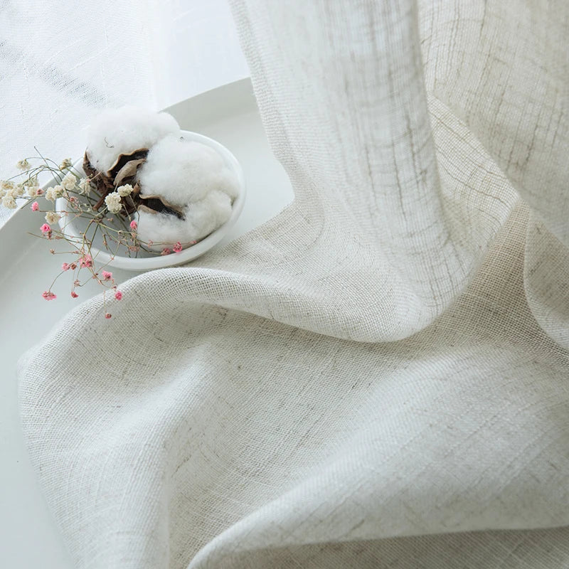 Rideaux élégamment drapés en lin et laine, démontrant l'art créatif du tissage. Les rideaux en matériaux naturels, affichent des nuances subtiles de couleurs pastel. Parfaits pour ajouter une touche cosy et artistique à toute pièce. Ce textile d'ameublement naturel sert également de toile de fond pour une table habillée d'une nappe en lin et entourée de serviettes assorties, soulignant l'importance du lin et de la laine dans la création d'intérieurs confortables et esthétiquement agréables.