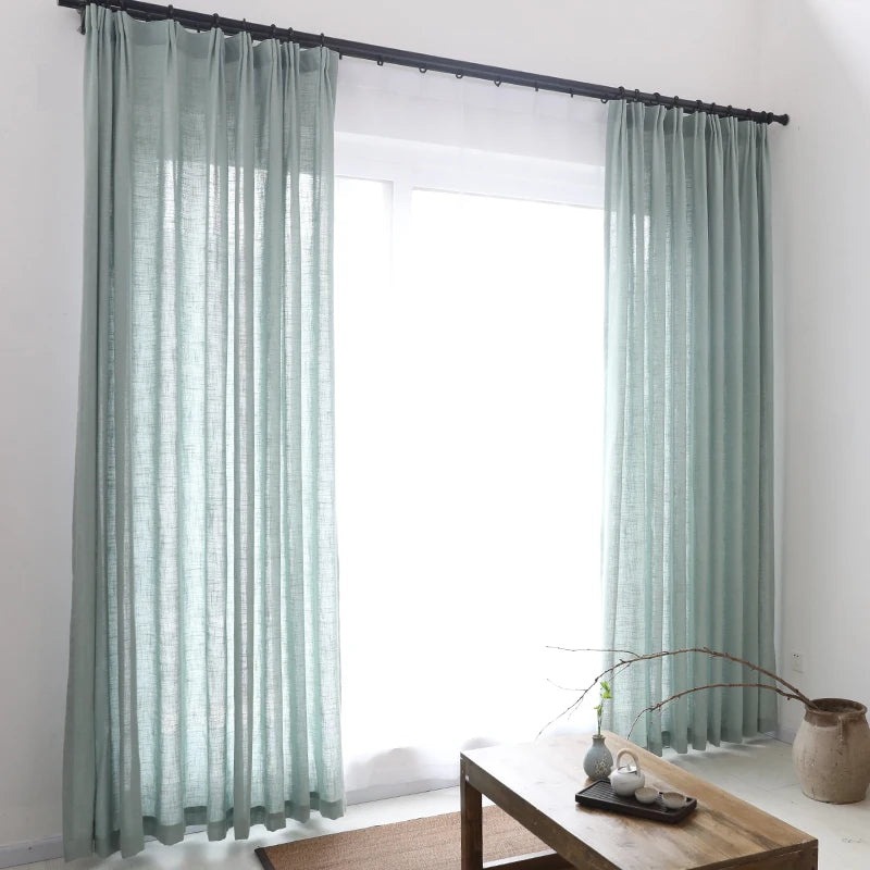 Zoom sur un rideau en tulle gris translucide avec texture tissée, suspendu à côté d’une chaise en bois clair.