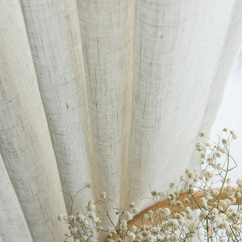 Gros plan sur un voilage effet lin naturel légèrement plissé, accompagné de fleurs séchées blanches pour une ambiance poétique.