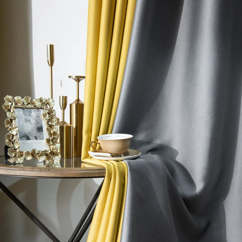 Détail du tissu des rideaux jaune moutarde et gris anthracite tombant élégamment sur une table dorée avec tasse et cadre décoratif.