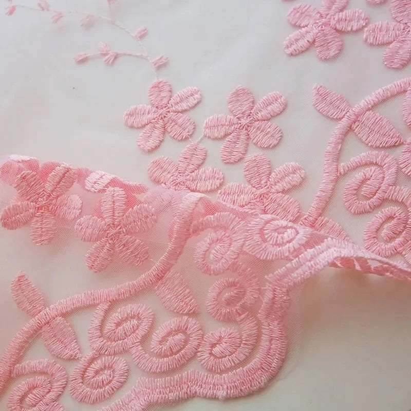 Gros plan sur les broderies florales roses du voilage transparent en tulle