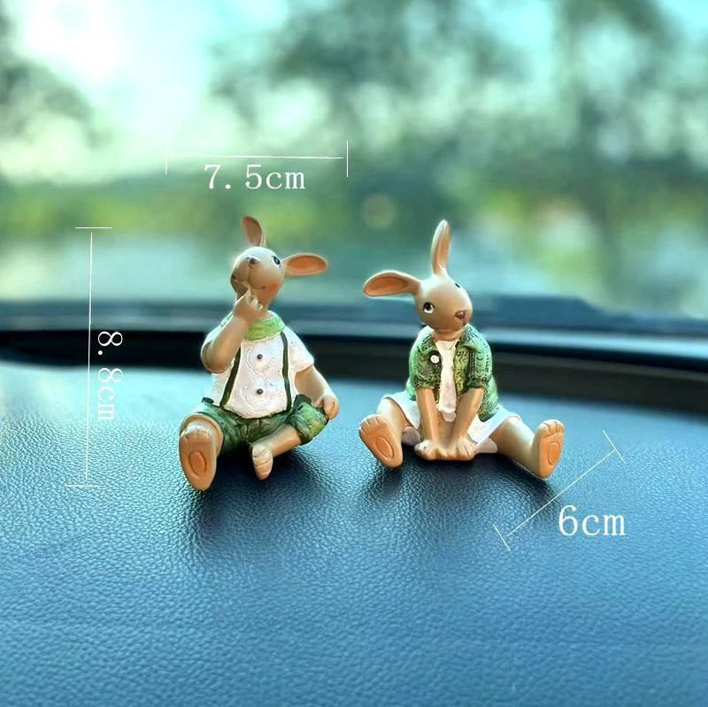 Deux lapins en céramique habillés de façon décontractée assis sur un tableau de bord de voiture.