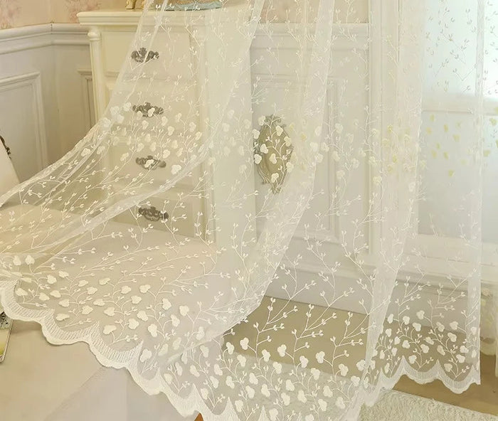 Voilage blanc cassé à motif floral drapé devant un meuble ancien de style baroque.