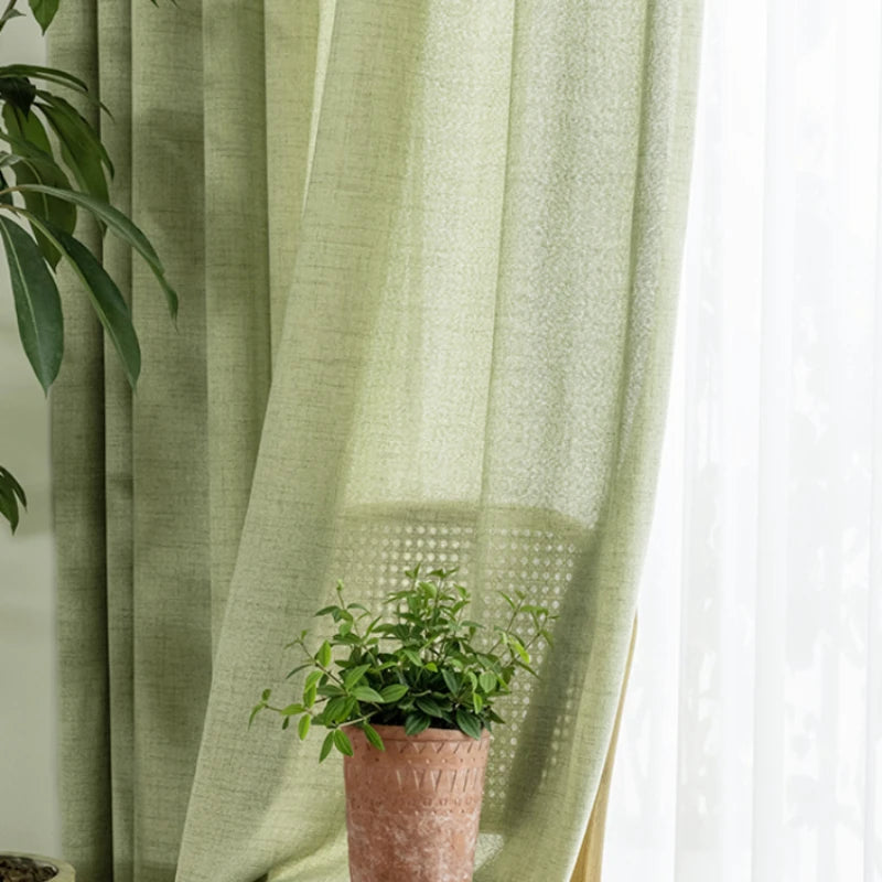 Rideau vert amande translucide laissant passer la lumière, décoré avec une plante dans un pot en terre cuite.