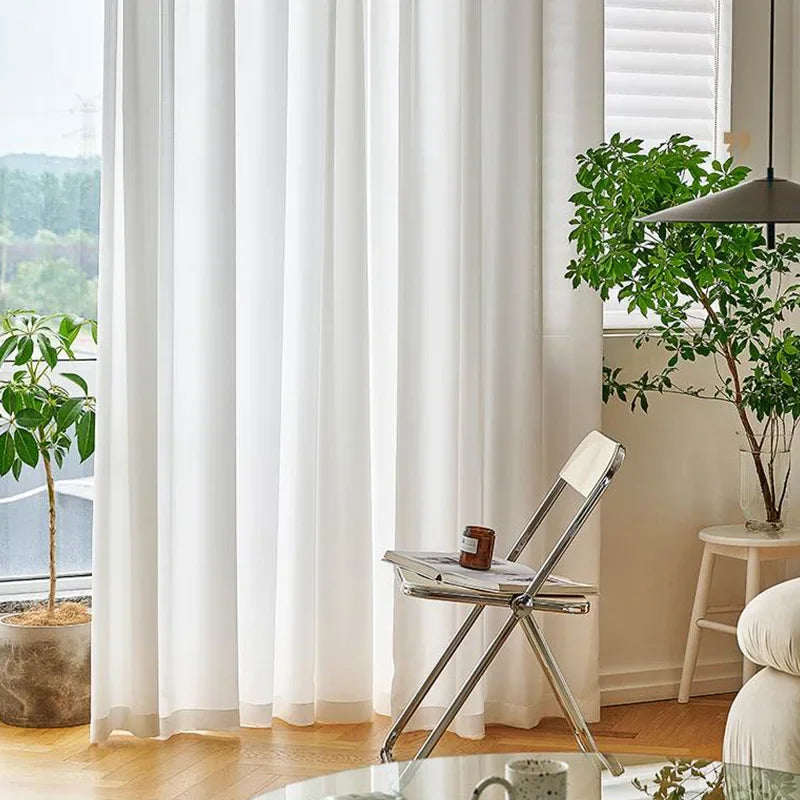 Voilage blanc élégant habillant une baie vitrée dans un salon lumineux décoré de plantes vertes et de mobilier minimaliste
