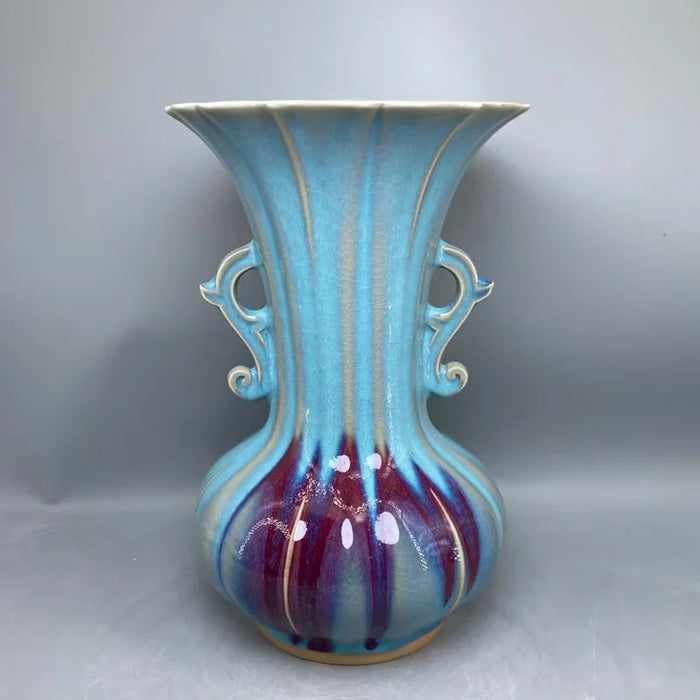 Le vase présente une forme élégante avec des ondulations de couleurs bleues et bordeaux, créant une harmonie visuelle attirante.