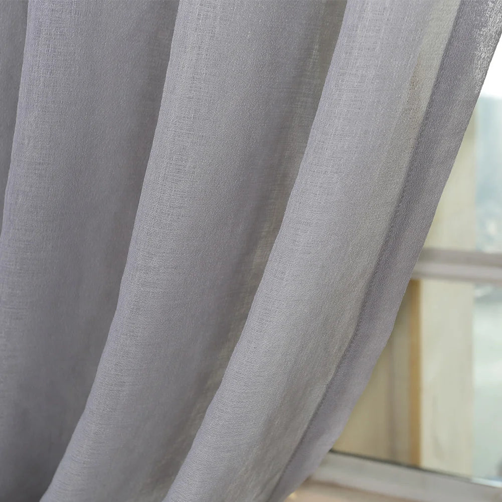 Image d'une élégante fenêtre habillée d'un traitement de fenêtre en textile, mettant en avant de magnifiques rideaux en lin gris argenté. Les rideaux possèdent des œillets pour une installation facile. La qualité supérieure utilisée pour ces rideaux est mise en évidence, apportant une touche raffinée à tout espace intérieur. Parfait pour ceux qui recherchent des accessoires de maison de luxe dans leurs draps et linges de maison.