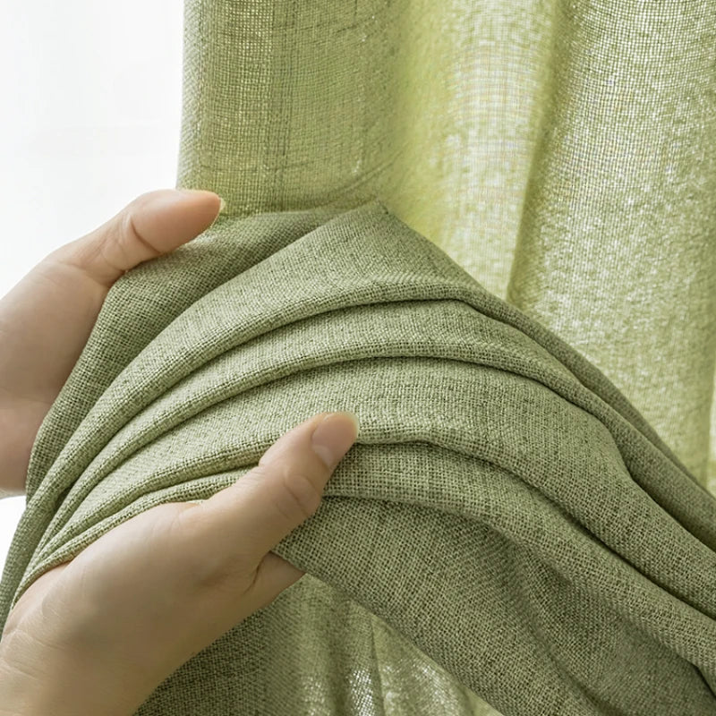 Zoom sur la texture épaisse et naturelle du rideau vert amande tenu dans une main.