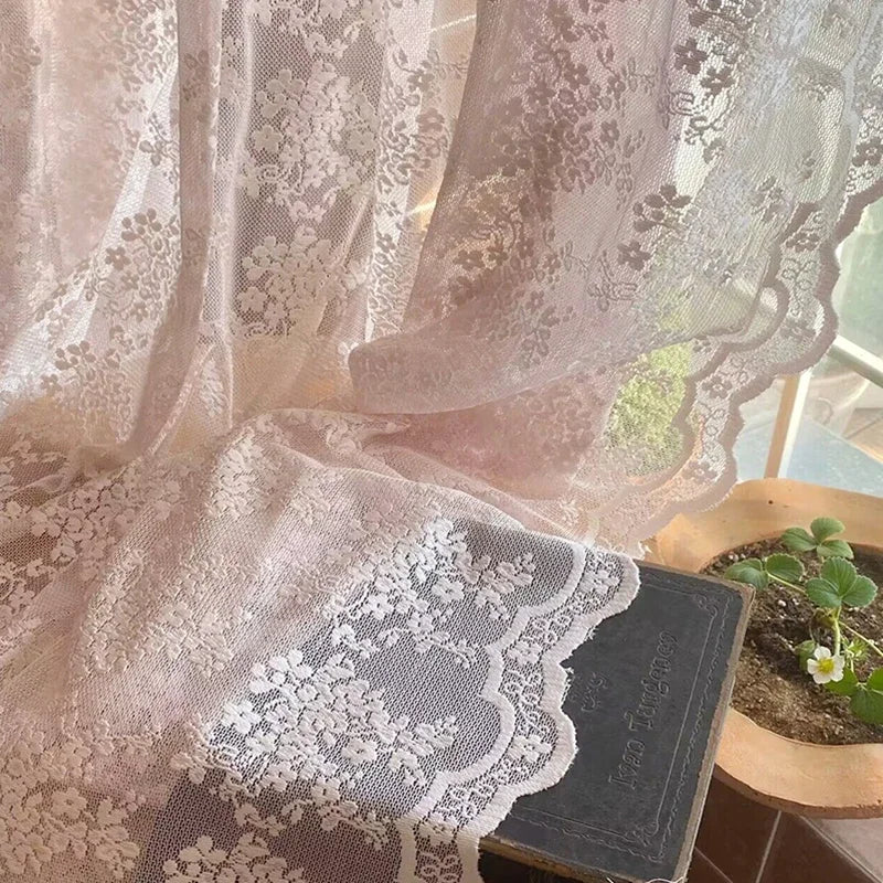 Détail du voilage rose en dentelle délicatement posé sur un livre ancien, laissant apparaître les motifs floraux en transparence.