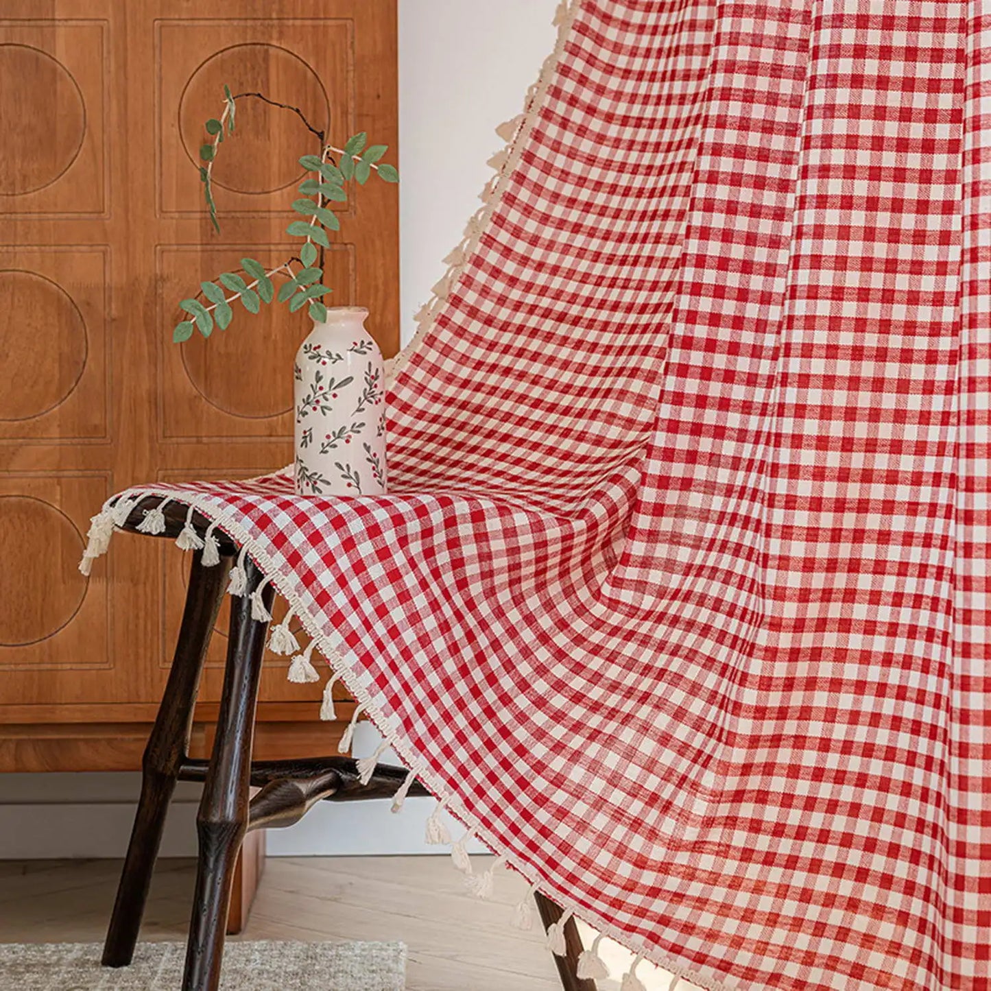 Plaid à carreaux rouges et blancs avec franges décoratives, idéal pour un salon chaleureux. Se marie parfaitement avec des meubles en bois, offrant une touche de charme rustique et élégant. Compagnon parfait pour les après-midis cocooning, ce plaid apporte confort et style.