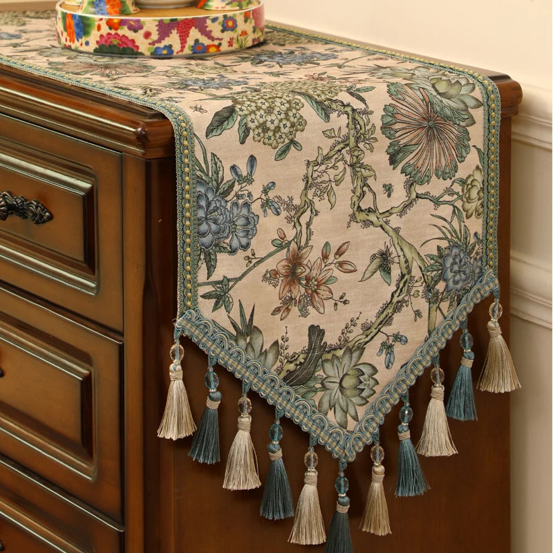 Magnifique chemin de table fleuri avec des motifs colorés et ornements de glands en tissu décorant avec élégance le meuble en bois.