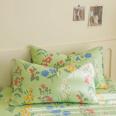 Couverture de lit verte avec un motif de fleurs colorées, créant une atmosphère fraîche et végétale dans la chambre.
