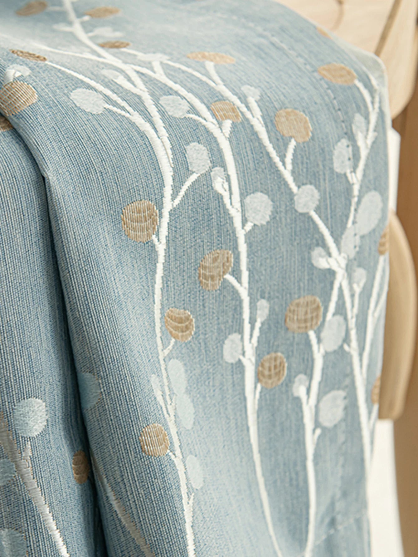 Détail du tissu d'un rideau occultant bleu en polyester avec motif floral brodé beige et blanc.