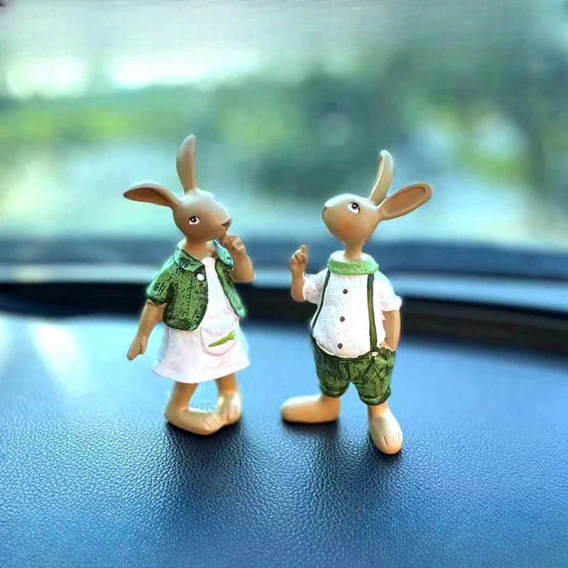 Deux adorables lapins en peluche habillés de tenues vertes se tiennent côte à côte sur le tableau de bord d'un véhicule, créant une scène mignonne et pittoresque.