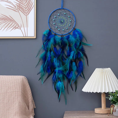 Capteur de rêves bleu et vert décoré de plumes dans un cadre intérieur aux murs gris.