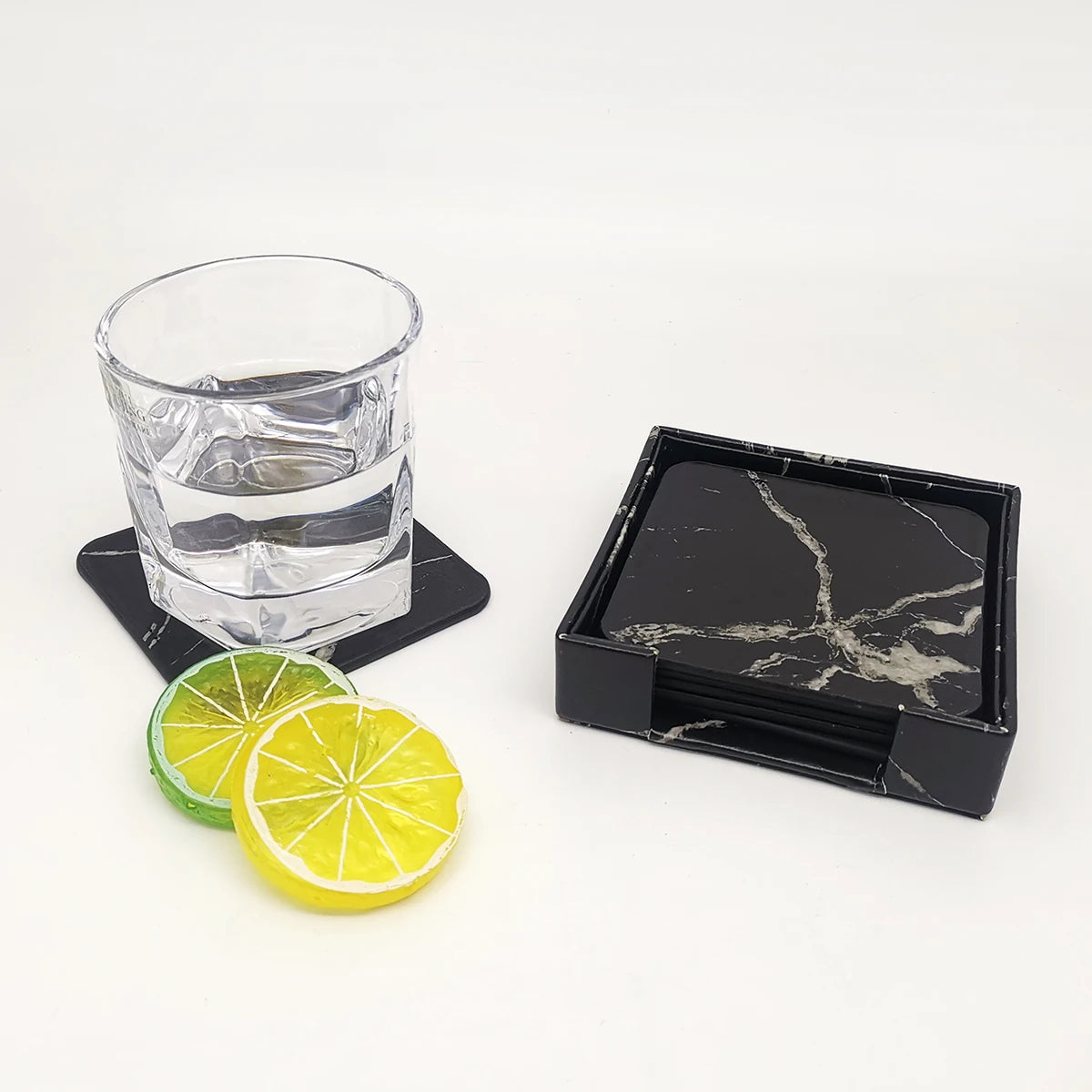 Un verre d'eau transparent avec des tranches de citron vert et jaune sur un support en pierre noire.