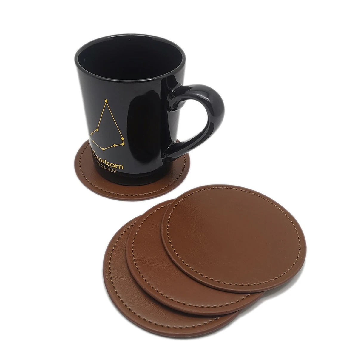 Une tasse noire en céramique avec le signe astrologique du Capricorne et des sous-verres en cuir marron foncé.