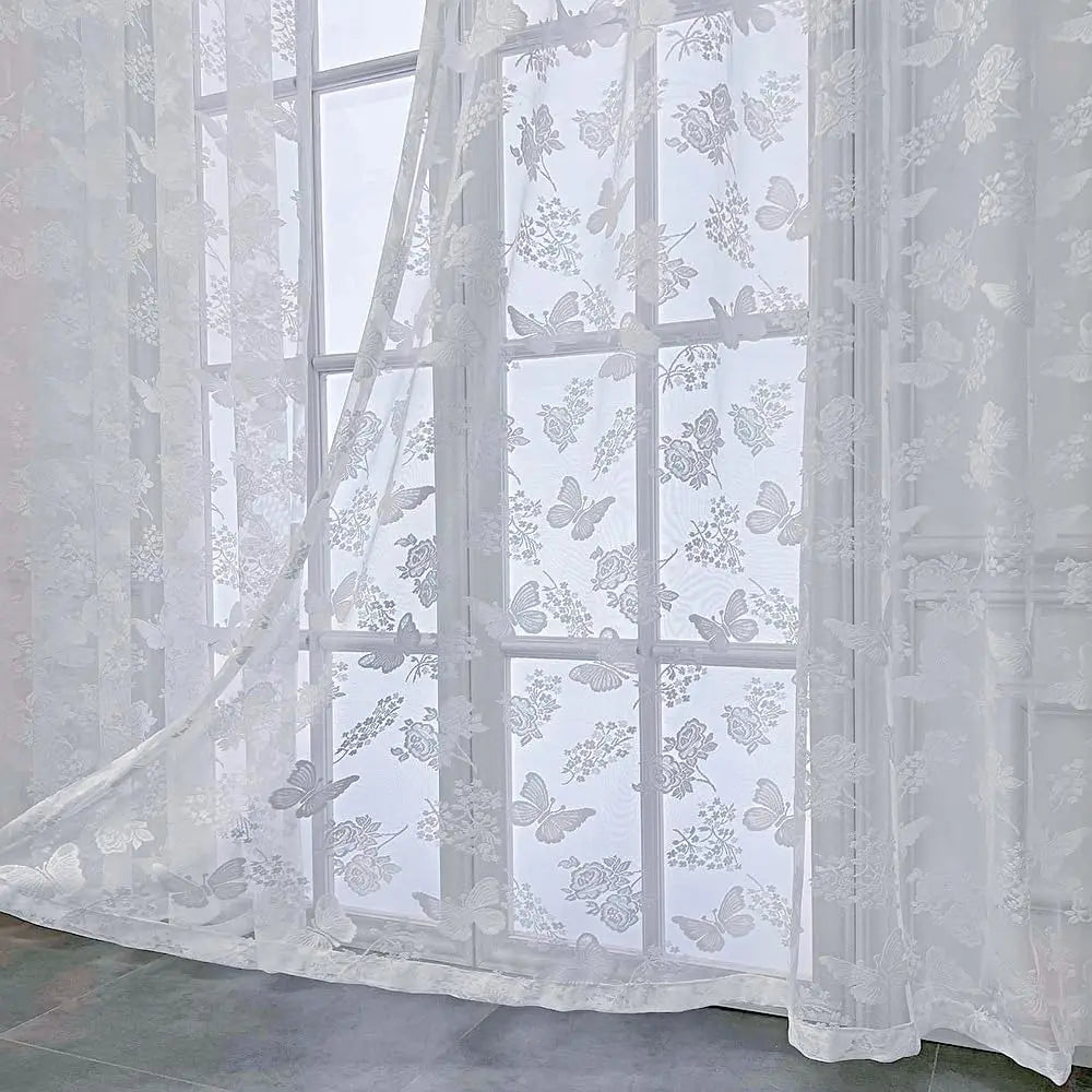 Voilage blanc transparent à motifs papillons et fleurs vu en gros plan dans une pièce lumineuse.
