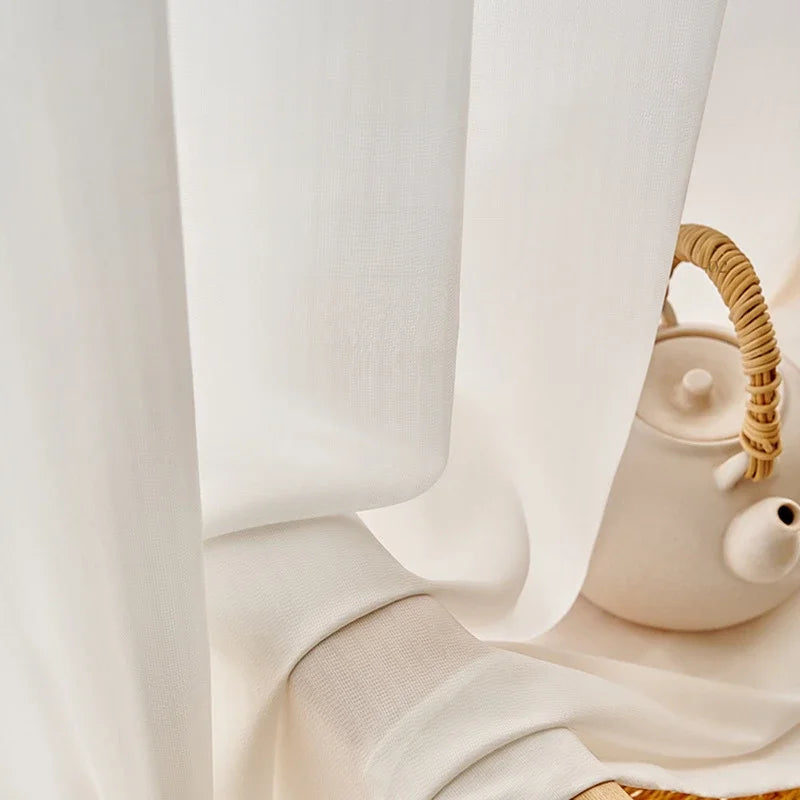 Détail du tissu du voilage blanc, délicatement posé sur le rebord d'une table avec une théière en céramique blanche