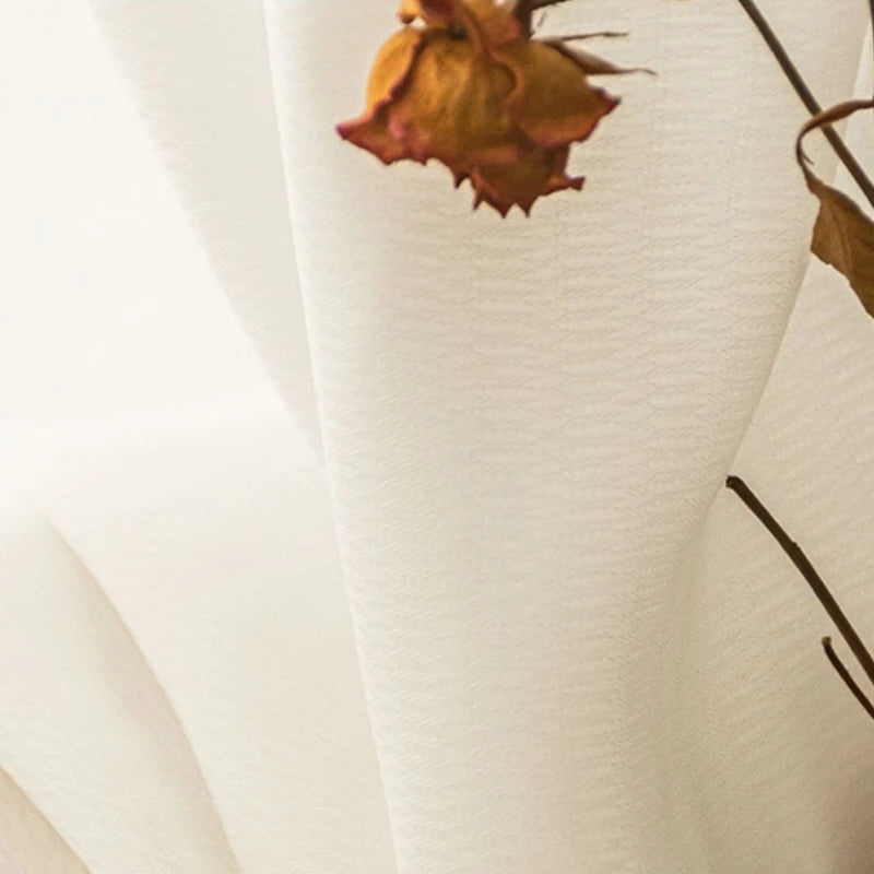 Gros plan sur la texture du voilage blanc avec une fleur séchée en arrière-plan, mettant en valeur la finesse et la légèreté du tissu.