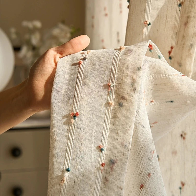 Gros plan sur le tissu du voilage montrant les détails de texture et les pois colorés brodés à la main.