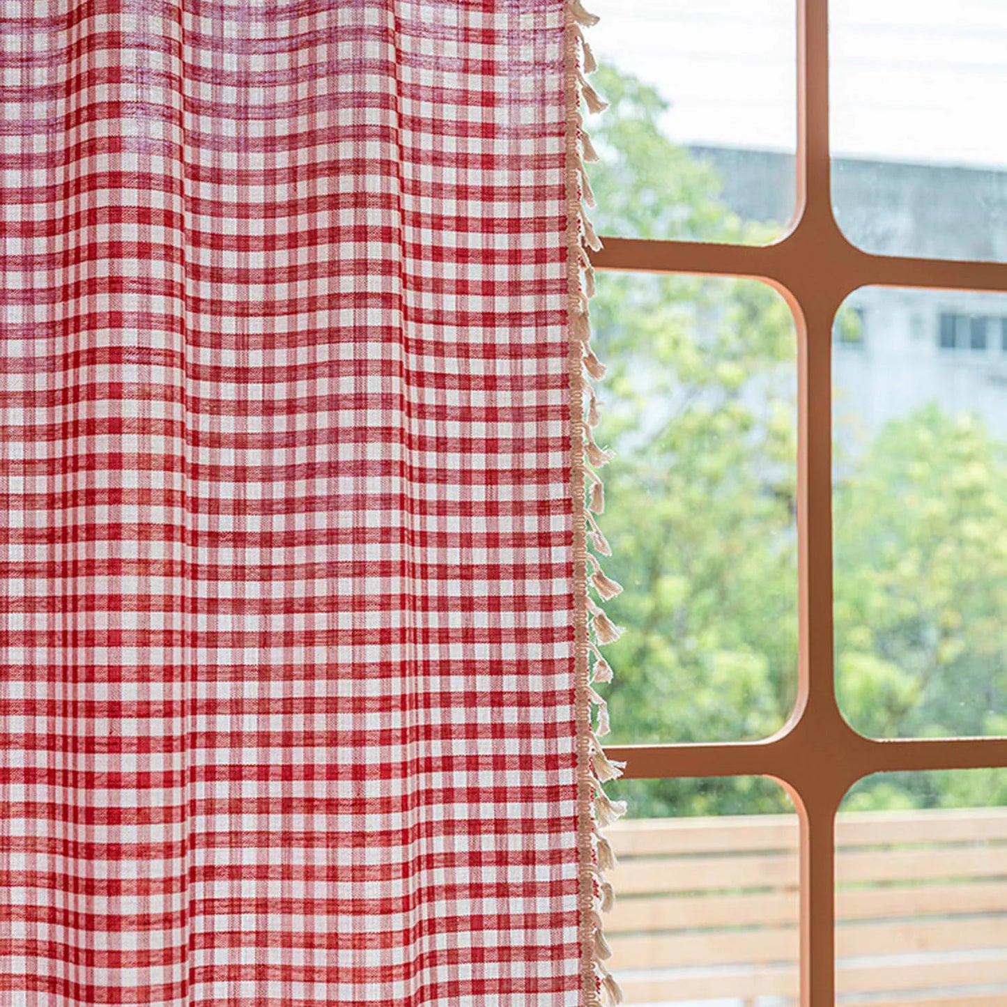 Rideau à carreaux rouges et blancs avec franges, suspendu près d'une fenêtre lumineuse. Parfait pour ajouter une touche de charme rustique à votre intérieur tout en offrant une touche de couleur vive à votre décoration.