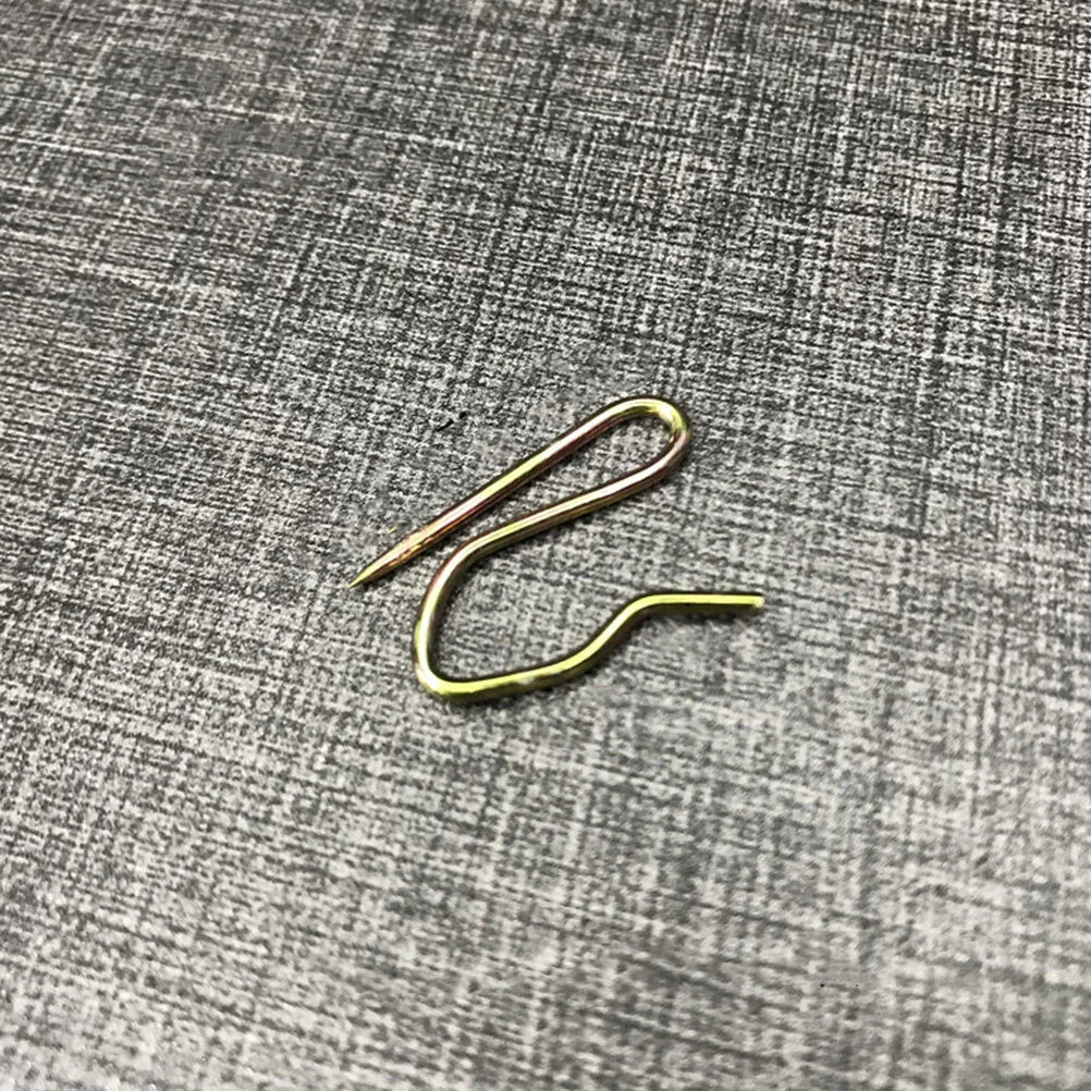 Un crochet à rideau en métal doré posé sur une surface grise texturée.