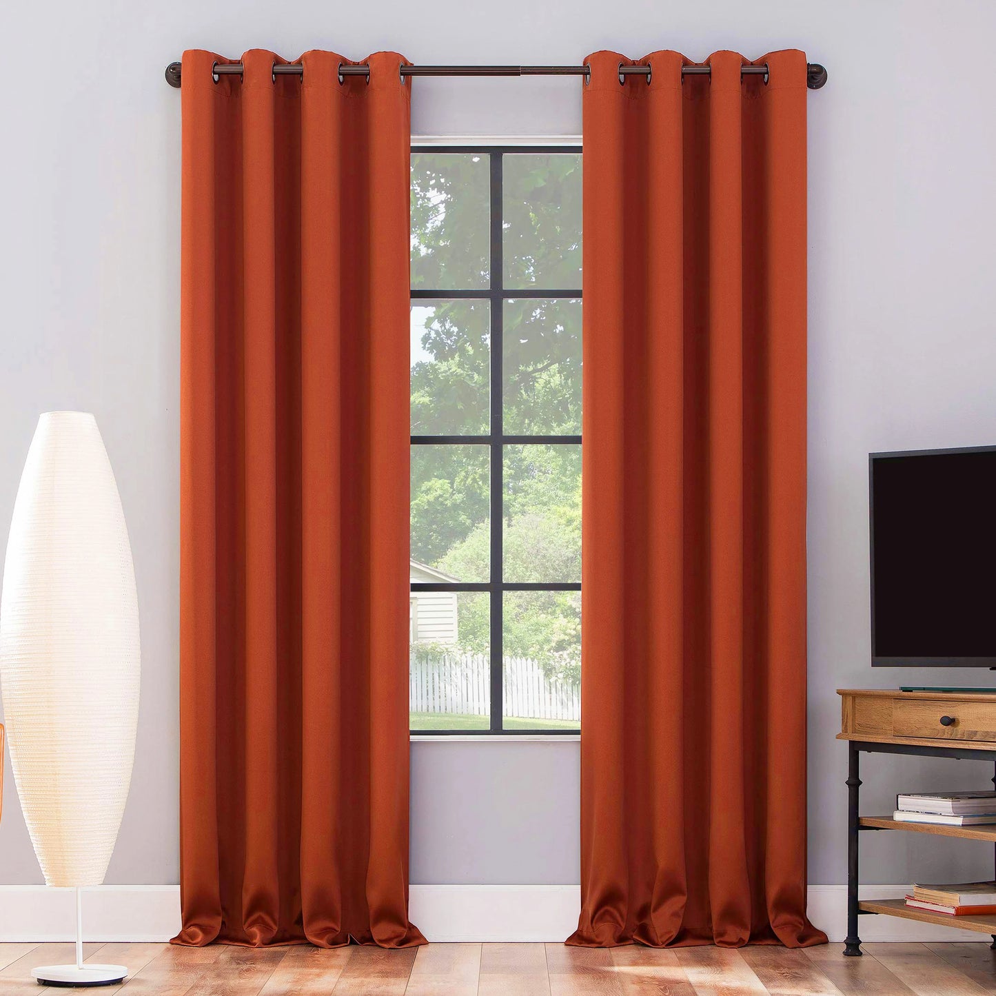 Rideaux drapés orange brûlé installés dans un salon moderne, encadrant une grande fenêtre à croisillons avec vue sur un jardin arboré.