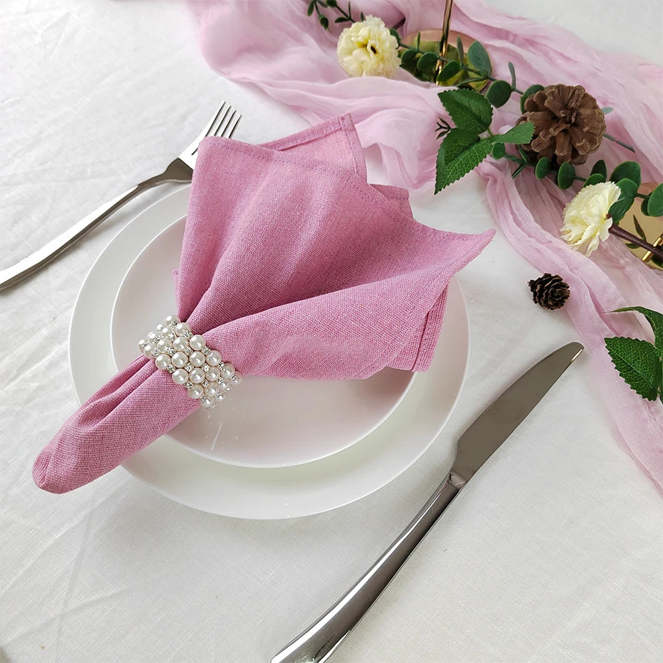 Une belle table de fête avec de délicates serviettes roses décorées de perles, entourées de fleurs fraîches et de pommes de pin, créant une atmosphère élégante et chaleureuse.