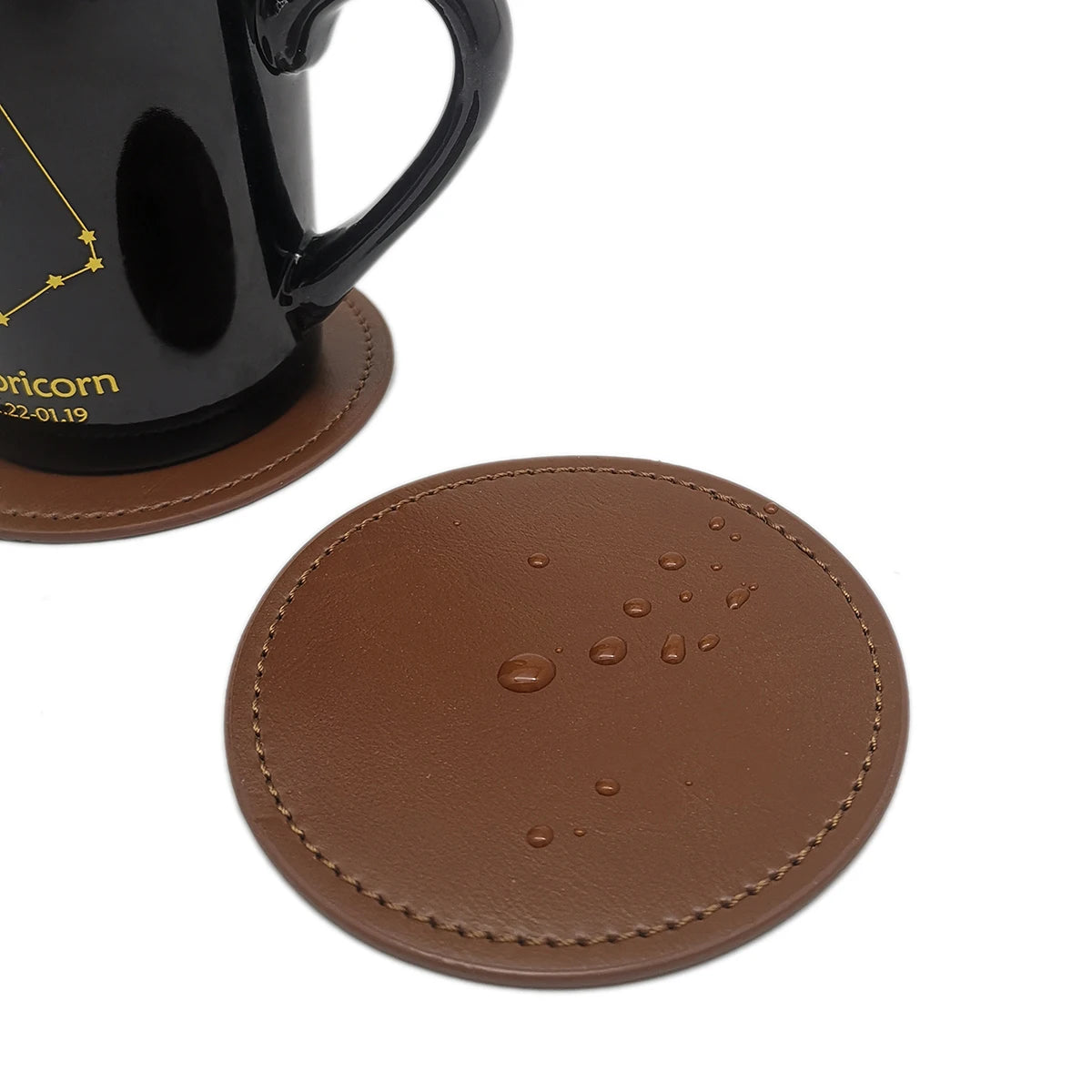 Un dessous de verre en cuir de couleur marron clair orné de gouttes d'eau, accompagné d'une tasse de café noire avec le signe du zodiaque du Capricorne.