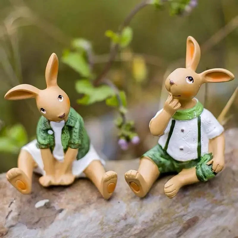 Deux lapins en peluche mignons portant des vêtements verts assis sur un sol en pierre avec des fleurs en arrière-plan.