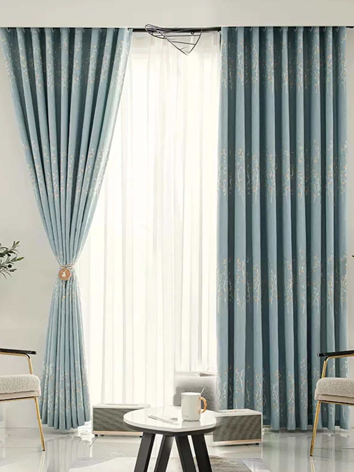Rideaux occultants bleus à motifs floraux installés dans un salon lumineux avec voilage blanc.