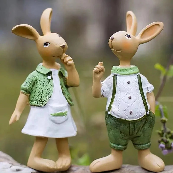 Deux adorables figurines de lapins mignons, vêtus de tenues casual et élégantes, posent dans un environnement verdoyant et bucolique.