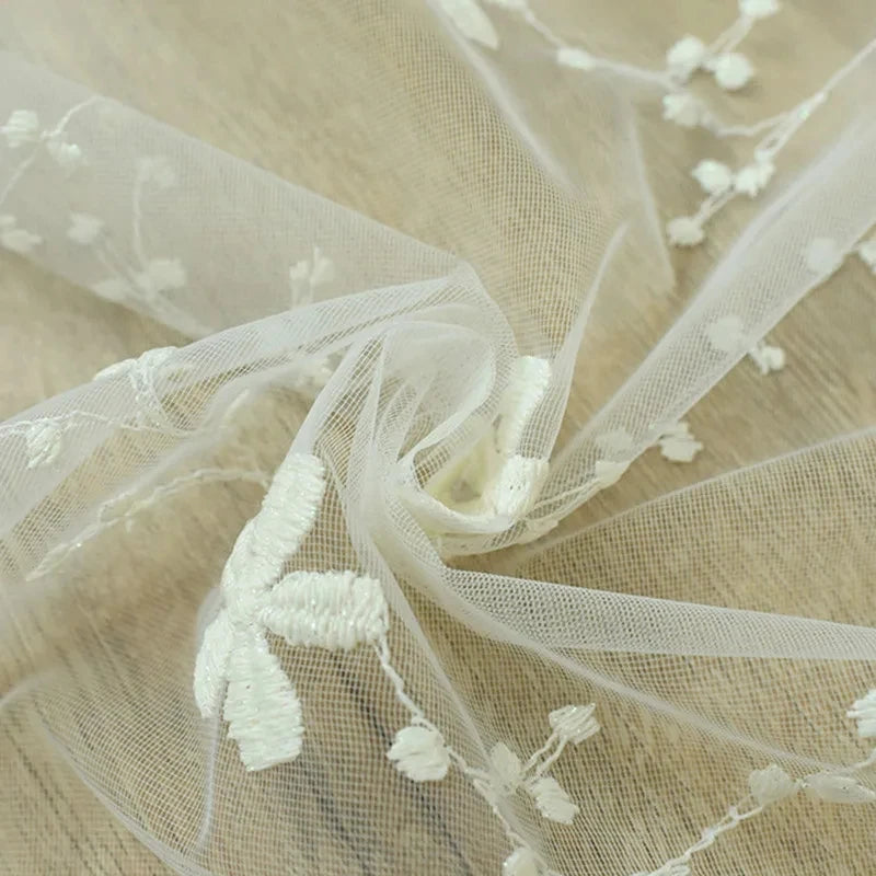 Zoom macro sur le tissu en maille fine du voilage blanc, mettant en valeur la broderie florale délicate et la transparence aérienne du textile.