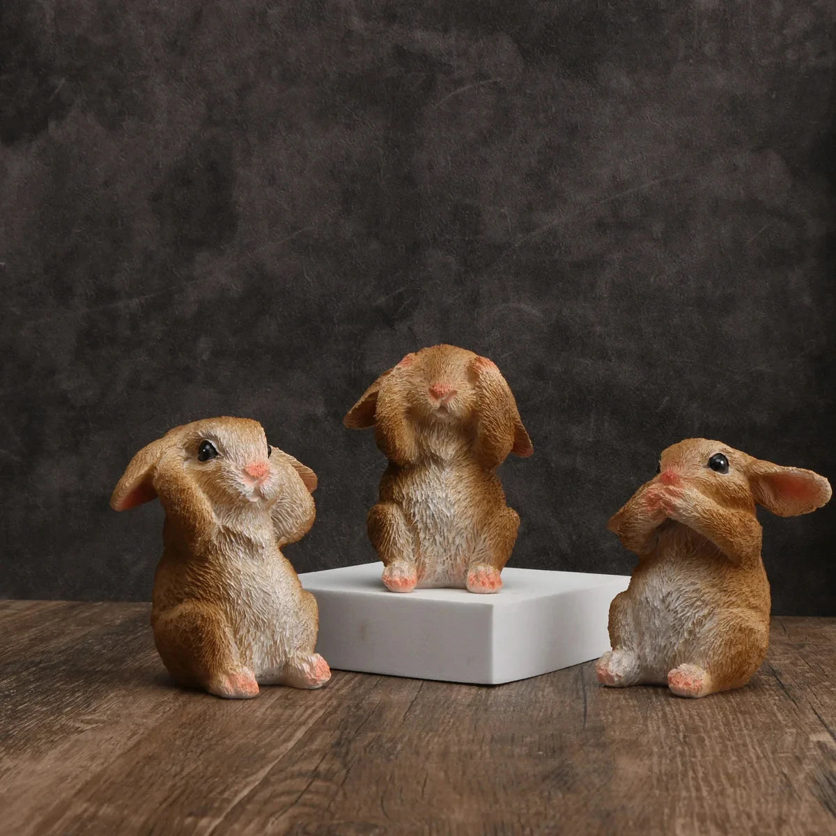 Trois lapins décoratifs assis sur un piédestal blanc sur fond sombre.