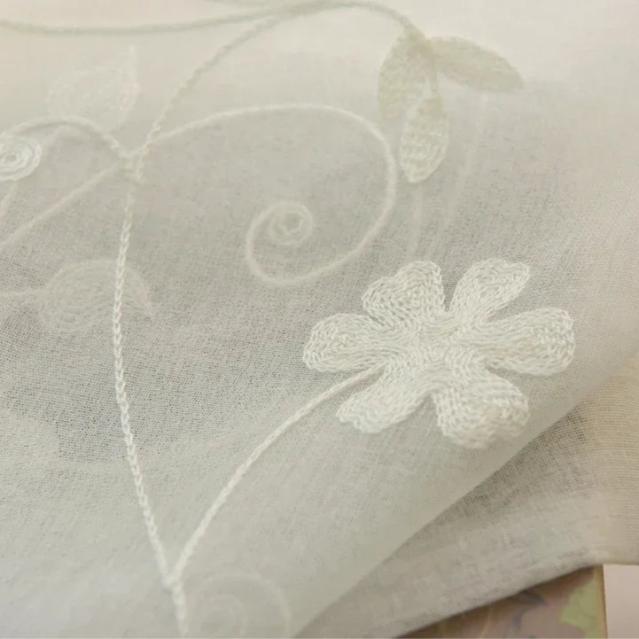 Des rideaux blanc et gris, ornés d'un motif créatif d'arts textiles, rappelant un papier peint ou une nappe en lin. Ces rideaux, avec leur broderie délicate, offrent une touche d'élégance et de style à toute pièce, tout en conservant la simplicité et le charme des textiles de maison.