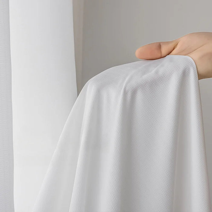 Main tenant un voilage blanc semi-transparent montrant la douceur du tissu.