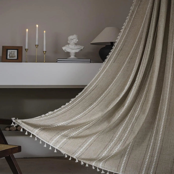 Voilage rayé beige à pompons décoratifs suspendu dans un salon au style bohème chic avec bougies et décoration classique.