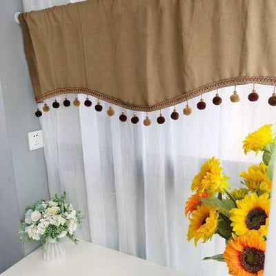 Cantonnière beige élégante avec pompons décoratifs, idéale pour ajouter une touche chaleureuse à votre intérieur. Parfaite pour les salons ou chambres, elle se marie bien avec les rideaux légers blancs en arrière-plan. Déco florale avec bouquet de tournesols et fleurs blanches pour une ambiance accueillante et naturelle.