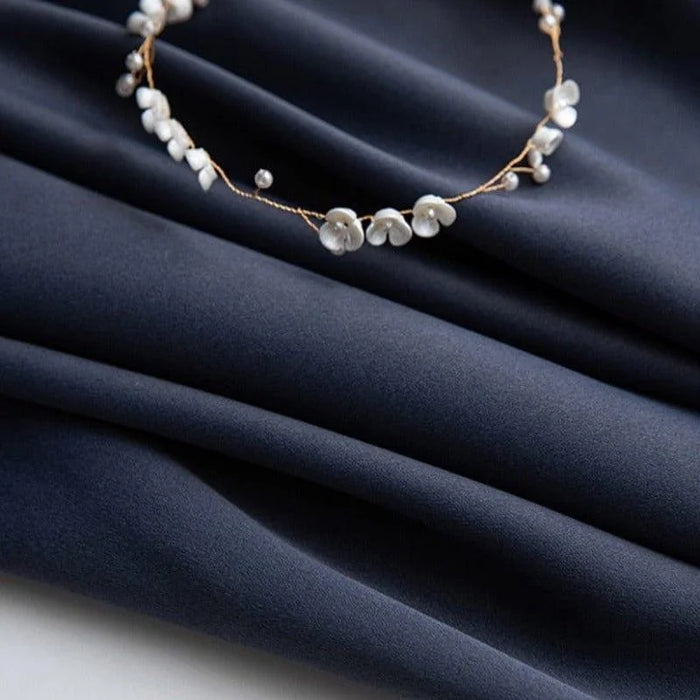 Image d'un tissu bleu foncé, délicatement orné d'un élégant bracelet de petites fleurs blanches, parfait pour créer une ambiance raffinée et sophistiquée dans vos créations textiles ou vos aménagements d'intérieur.