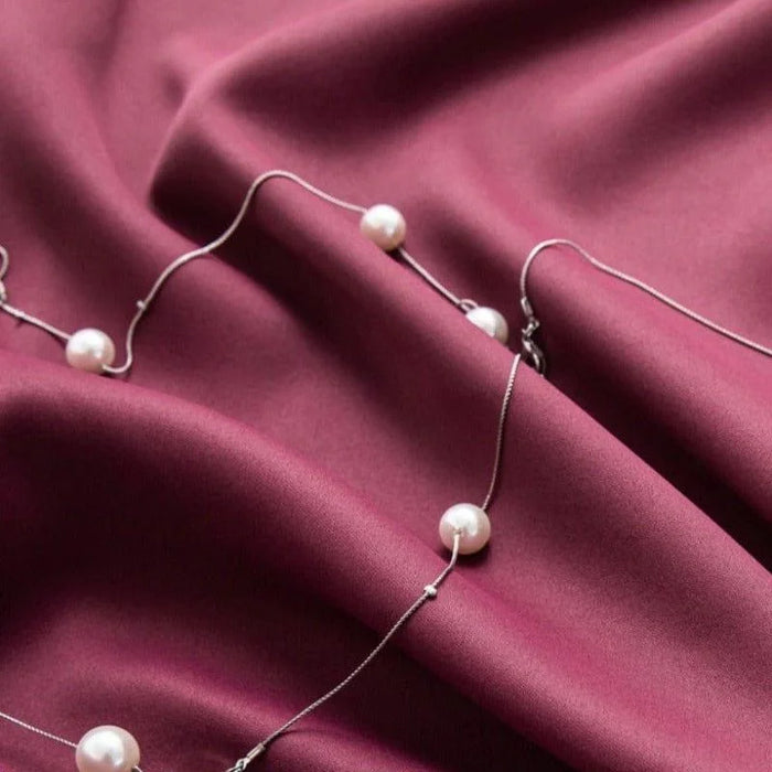 Collier élégant avec perles posé délicatement sur un tissu violet foncé. Accessoire de mode sophistiqué idéal pour compléter une tenue chic et raffinée. Parfait pour des occasions spéciales ou des soirées habillées.