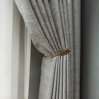 Rideau élégant de couleur grise avec motif discret, retenu par un embrasse doré en forme de feuille, idéal pour une décoration intérieure raffinée et moderne. Convient parfaitement pour les salons ou chambres à la recherche d'une touche de sophistication.