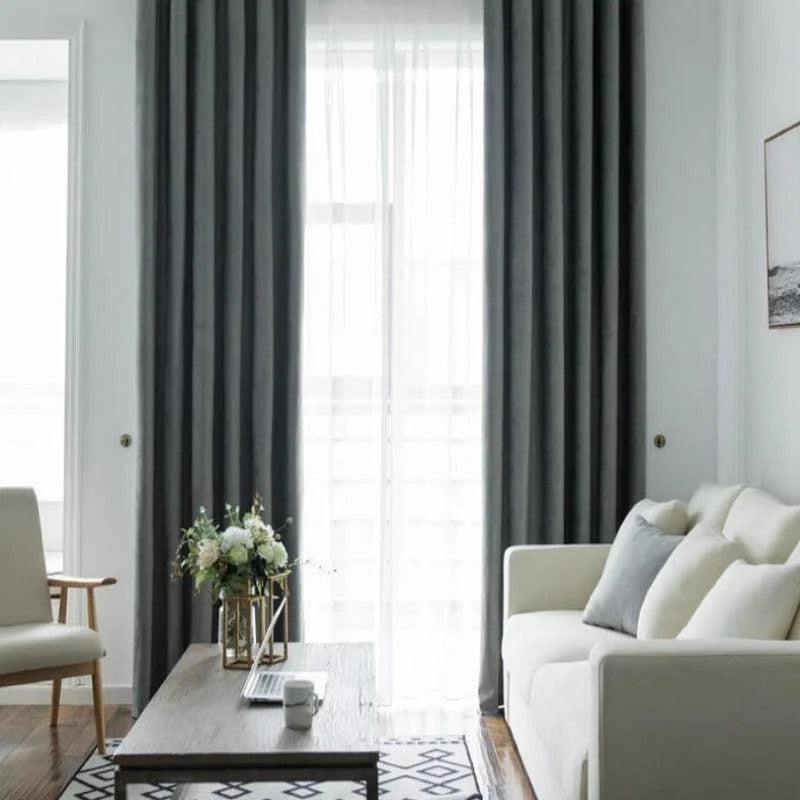 Salon moderne et élégant avec canapé blanc, rideaux gris et table basse en bois. Décoration harmonieuse avec coussins confortables et vase de fleurs fraîches. Idéal pour créer une ambiance chaleureuse et accueillante dans votre intérieur.