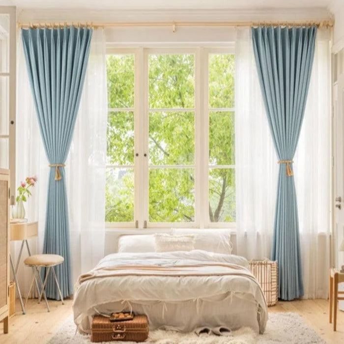 Chambre lumineuse avec grandes fenêtres habillées de rideaux bleus élégants, invitant à la détente et au confort. Ambiance naturelle et apaisante avec vue verdoyante. Rideaux parfaits pour un style moderne et raffiné, idéal pour rehausser la décoration intérieure.