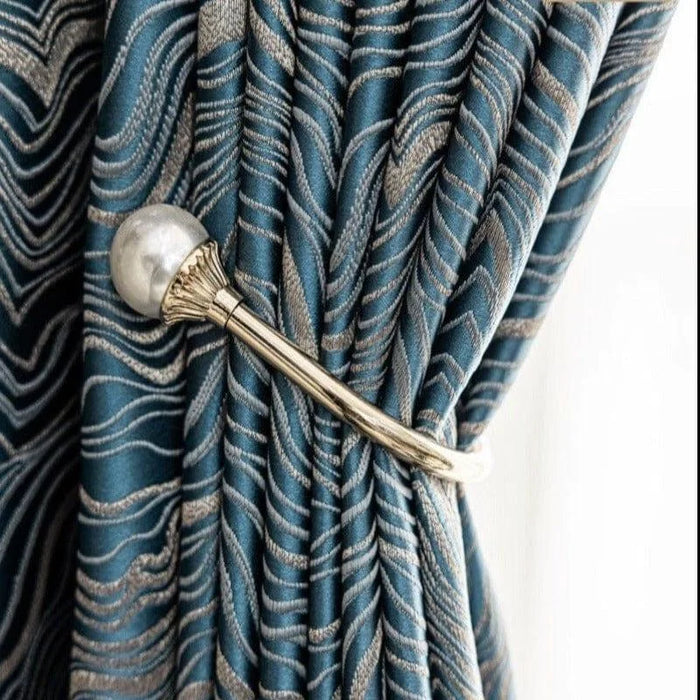 Rideau élégant avec motif ondulé bleu et argenté, attaché par une embrasse métallique dorée ornée d'une perle, idéal pour une décoration intérieure moderne et sophistiquée. Accessoire de fenêtre chic ajoutant une touche de luxe au salon ou à la chambre.