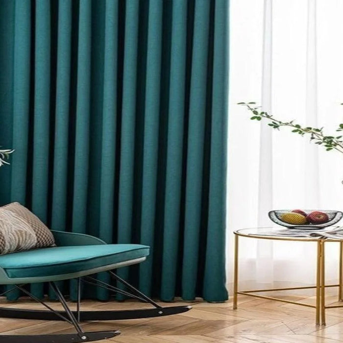 Rideaux élégants vert émeraude dans un salon moderne avec fauteuil à bascule assorti et table d'appoint dorée, lumière naturelle filtrée pour une ambiance chaleureuse et raffinée.