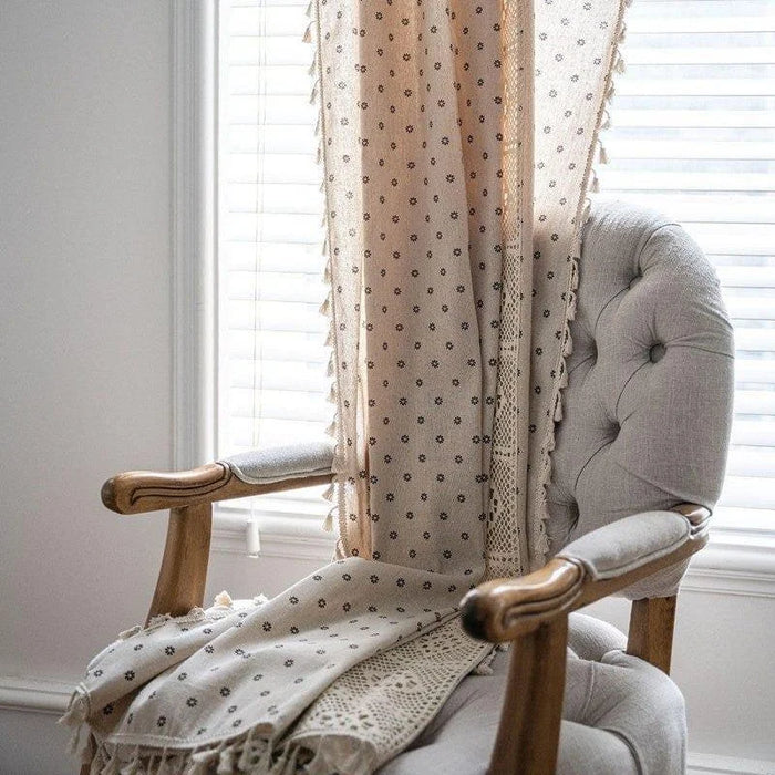Rideau décoratif beige à motifs floraux suspendu devant une fenêtre avec store, ajoutant une touche élégante à une chaise capitonnée avec accoudoirs en bois dans un intérieur lumineux. Idéal pour une ambiance chaleureuse et accueillante.